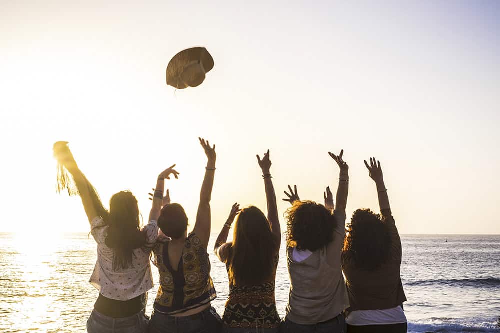 Summer and happiness for travel and freindship concept with group of happy girls viewed from rear enjoying and celebrating the sunset and the sea together launching hat and giving up